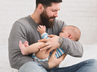 Image of a bearded dad cuddling in a crying baby. Dad looks stressed.